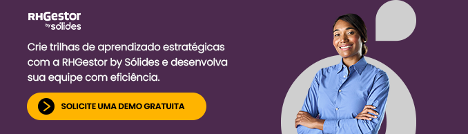 mulher de braços cruzados vestindo uma camisa azul claro e sorrindo em frente e um fundo roxo